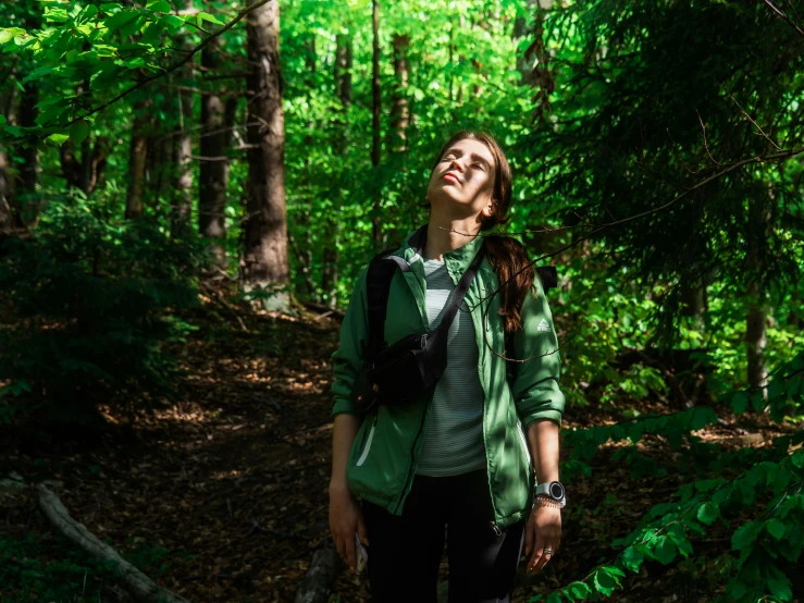 a woman with a backpack is looking up at the trees