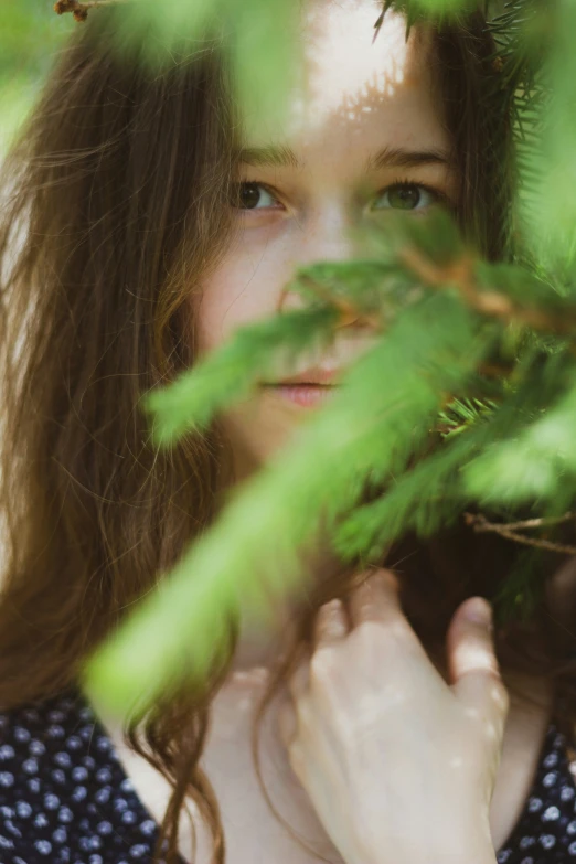 a young woman is smiling as she hides behind the leaves of a tree