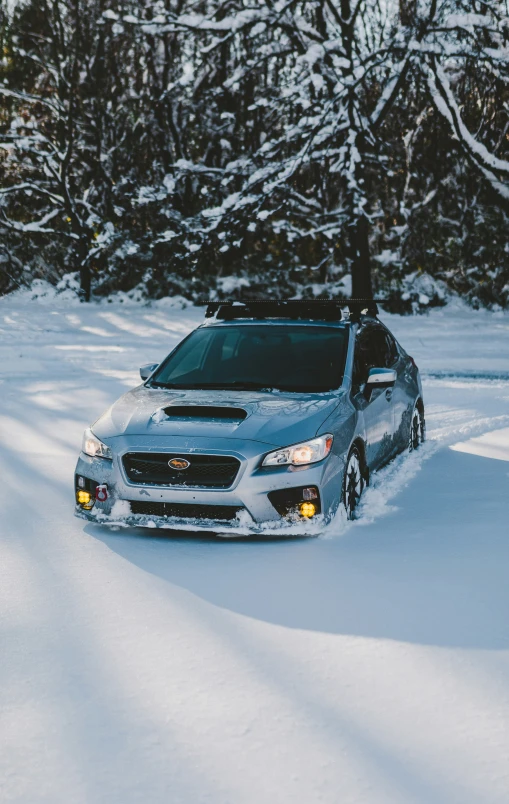 a silver subarunt with a black and white snow tailpipe stands in the middle of a snowy landscape