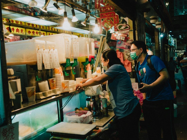 two people with masks standing behind a food stand