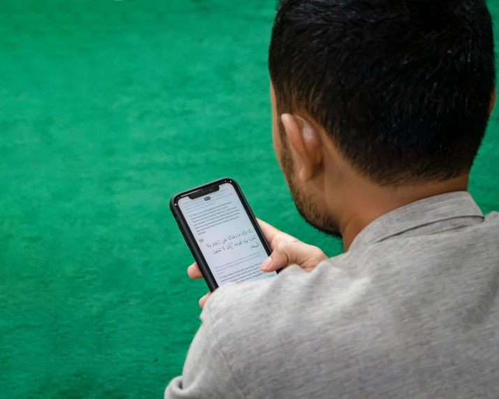 a man holding a cell phone looking at an image of a dog on green carpet