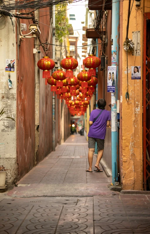 an elderly person walks through a narrow street with lanterns on the buildings