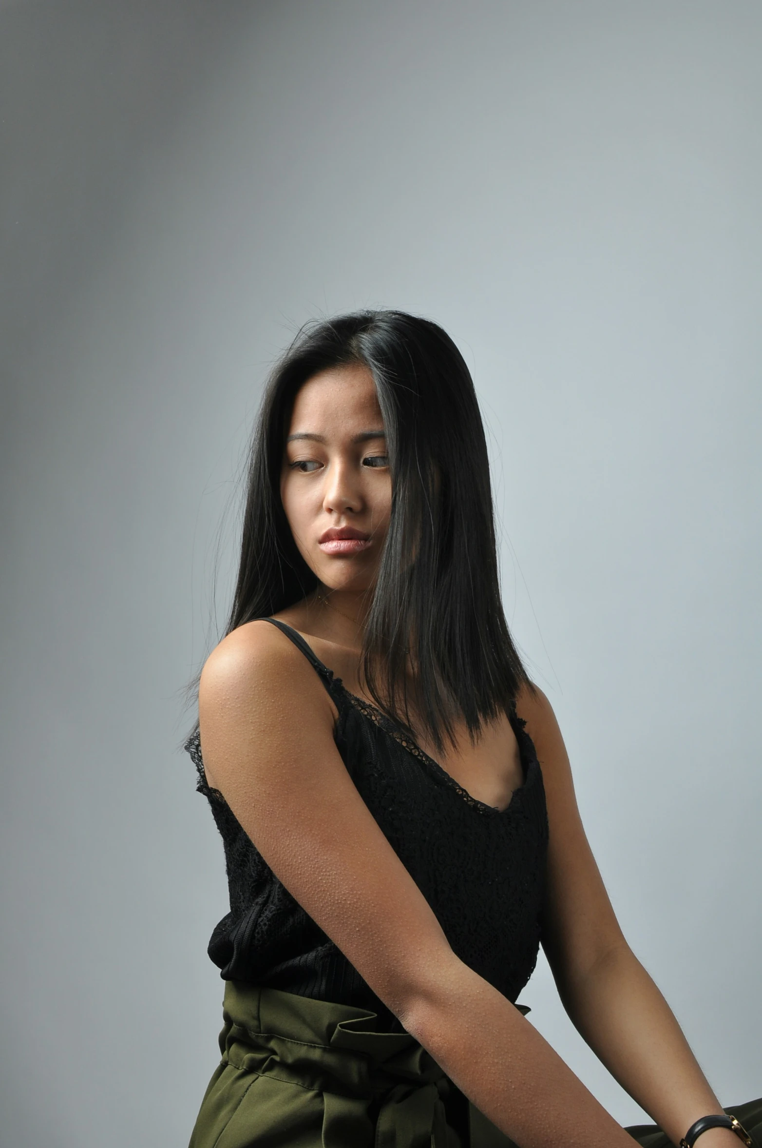 an asian woman sitting on a stool wearing her black shirt and green shorts