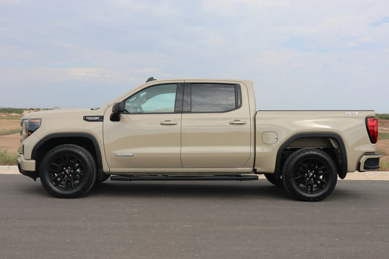 a tan truck with some black wheels parked by a field