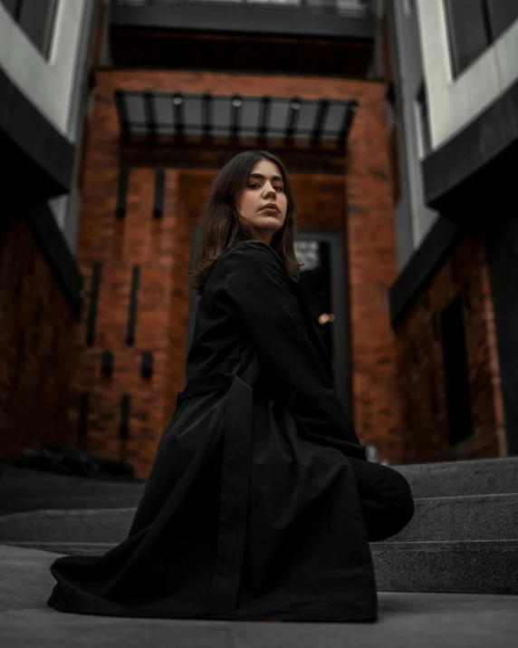 a person sits on steps in a black dress and looks up