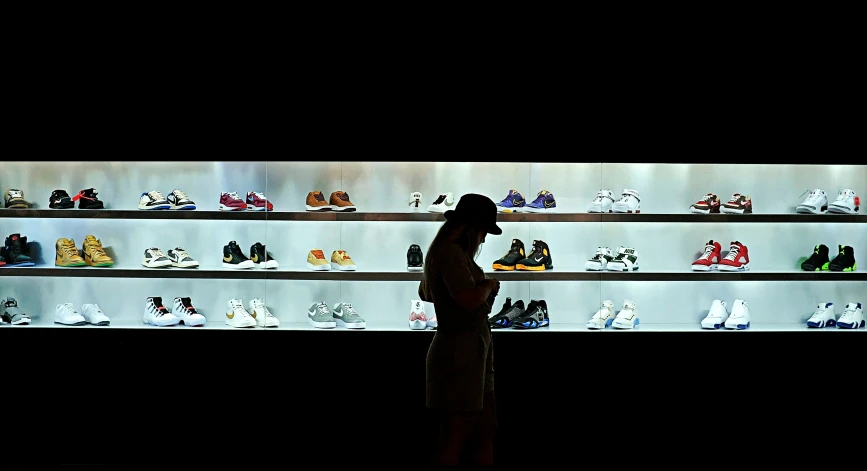 a woman looks at her cell phone while standing in front of a wall of shoes