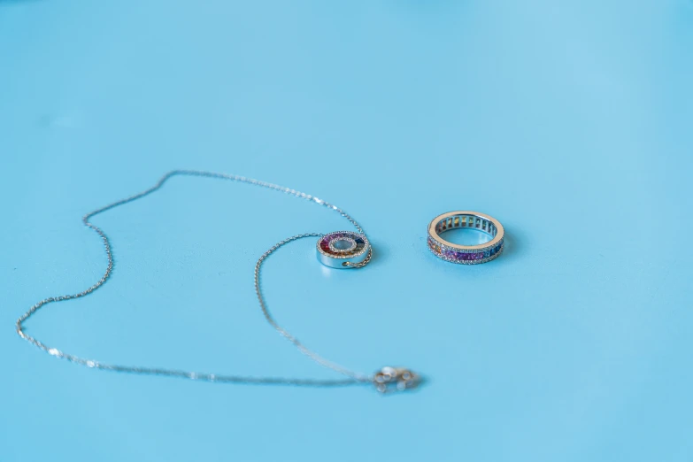 two rings laying on a light blue surface, one with a necklace and the other with a diamond ring