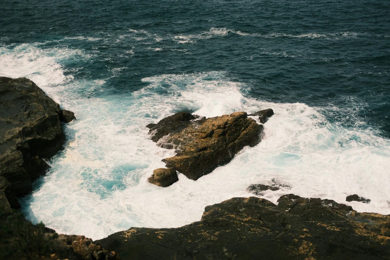 two people standing on rocks watching the ocean