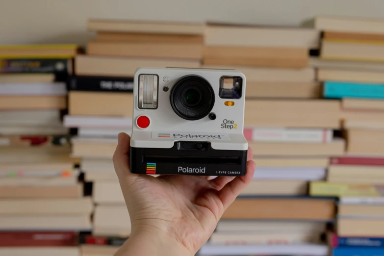 someone is holding a polaroid on top of stacks of books