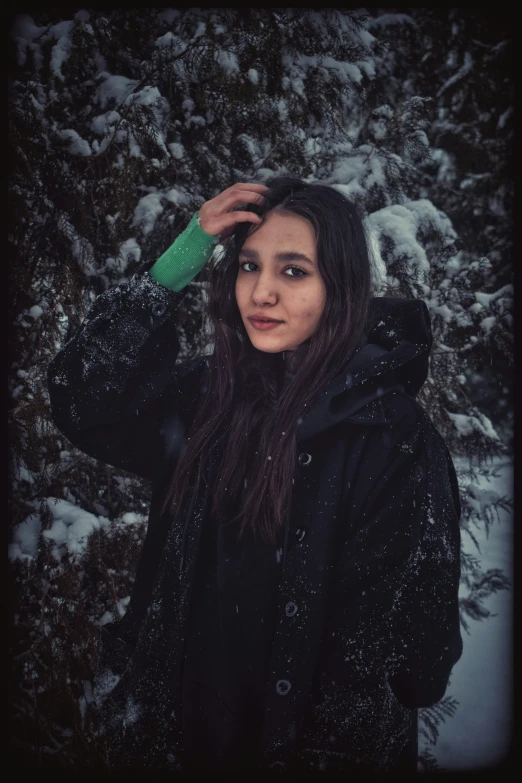 a  in a jacket and beanie hat holding a green handbag stands in a snow - covered forest