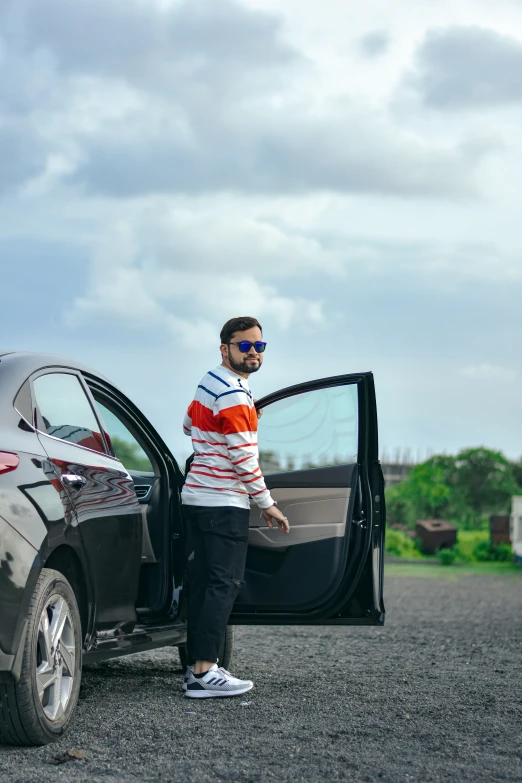 a man standing next to a black car on a gravel road