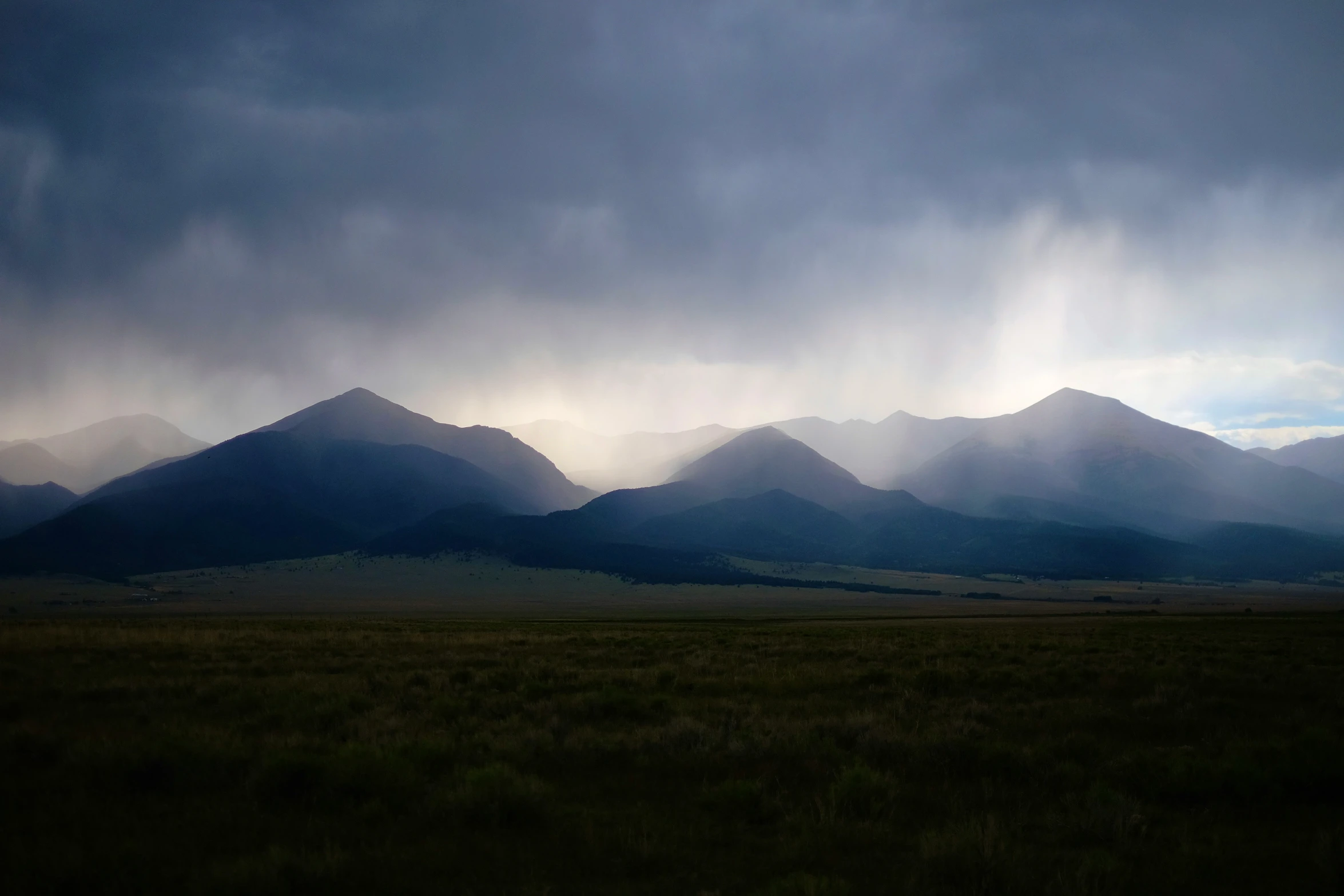 a field with grass on the side and mountains in the back