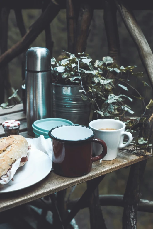 a table with two coffee mugs and a sandwich