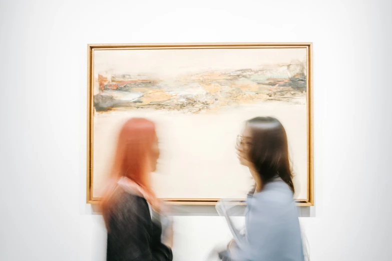 two women walking towards a painting in a white room