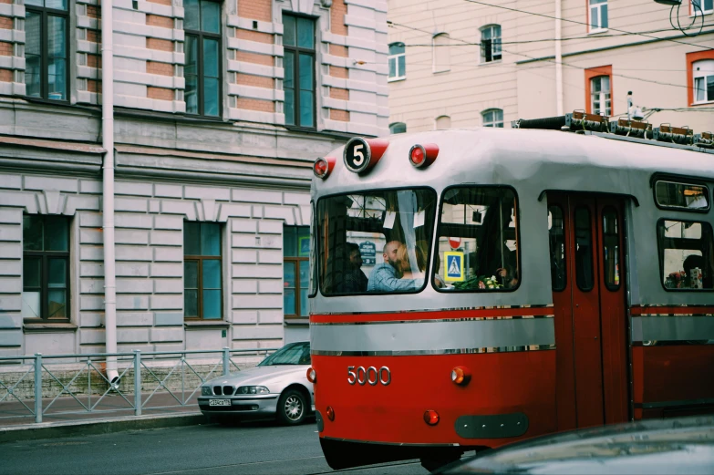 an old red and silver passenger tram traveling past tall buildings