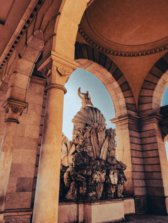 a golden fountain is located in an arched courtyard with stone pillars