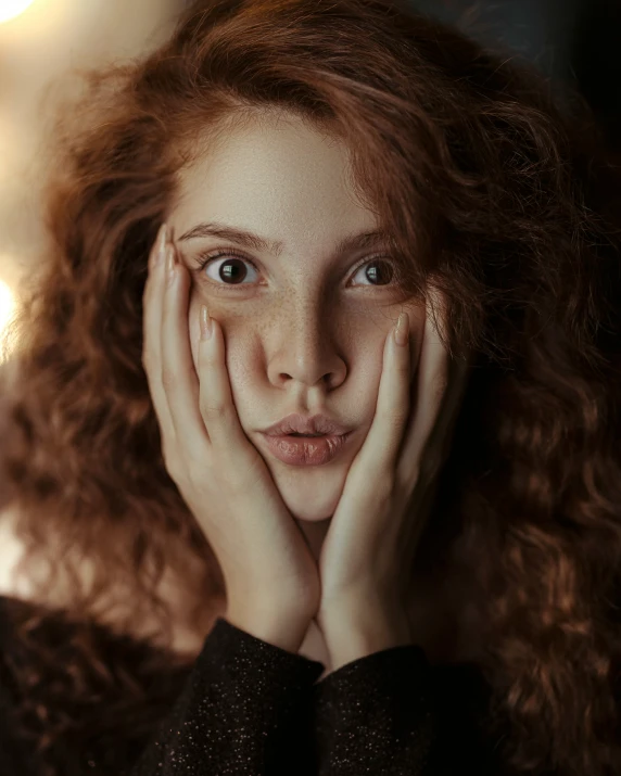 a young red haired woman with her hands near her face