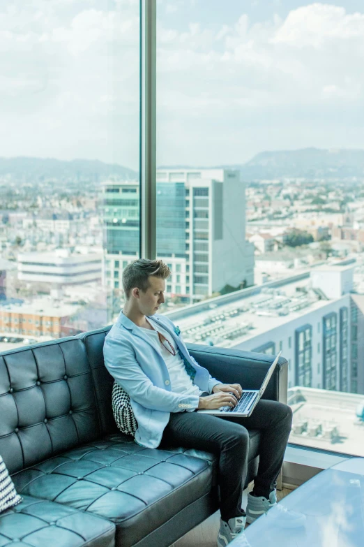 a man sitting on top of a couch working on a laptop