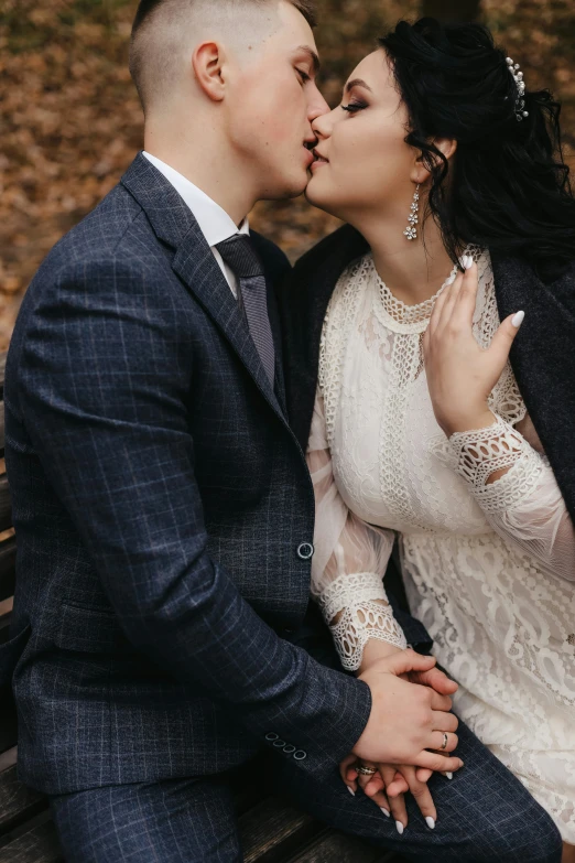 the bride and groom are kissing on a bench in the woods