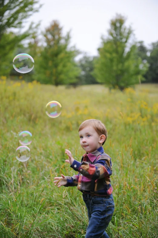 a little boy in a field has soap bubbles flying in the air
