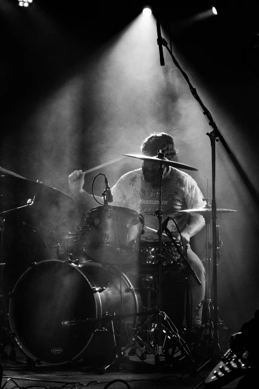 two drummers play their instruments on stage with light streaming in