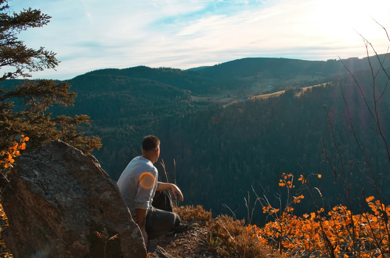 a man sitting on top of a hill looking out at mountains