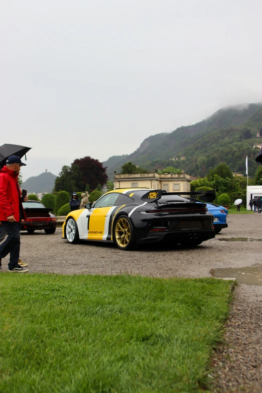 some people walking by some cars on a grassy field