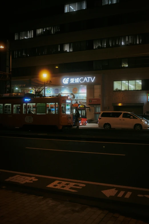a city street at night with a bus pulling up to the side of a building
