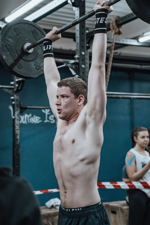 a shirtless man holding a barbell during a crossfit competition