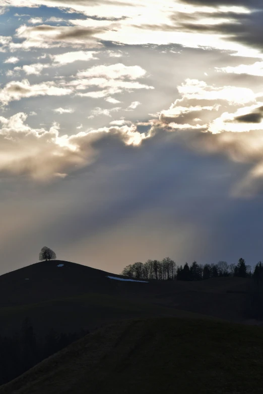 a sunset shines through the clouds on top of a hill