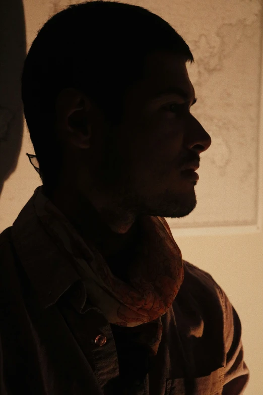 a man standing up in the shadows, wearing a scarf