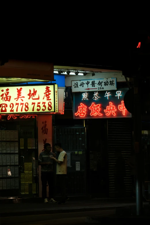 two people standing outside of an oriental restaurant at night