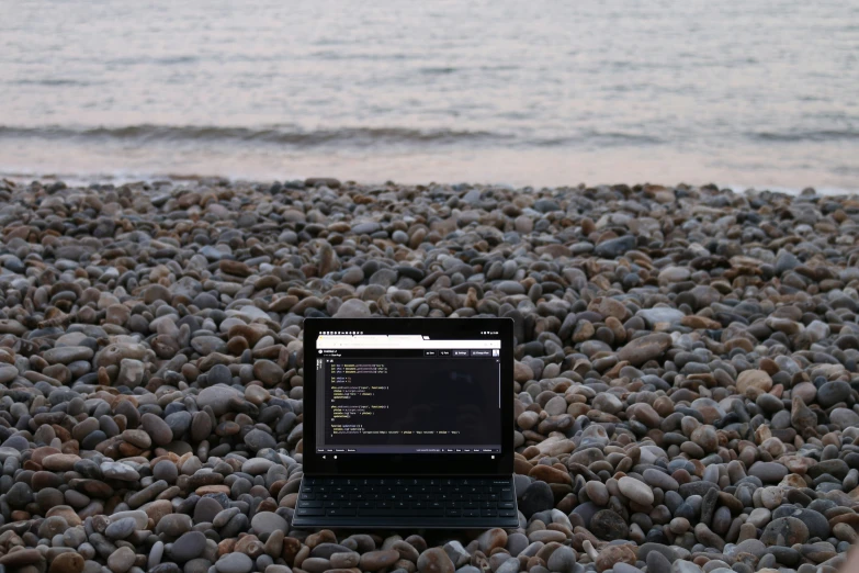 a laptop computer sitting on top of a rocky beach