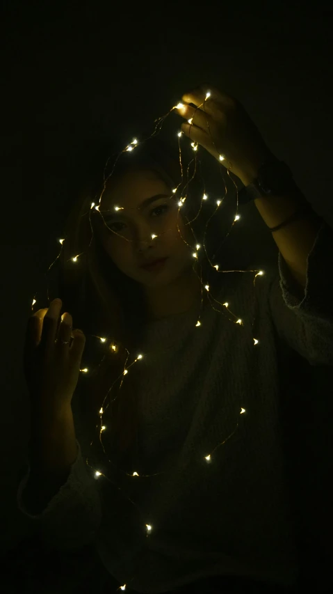 a woman is posing with her hands on her head with fairy lights