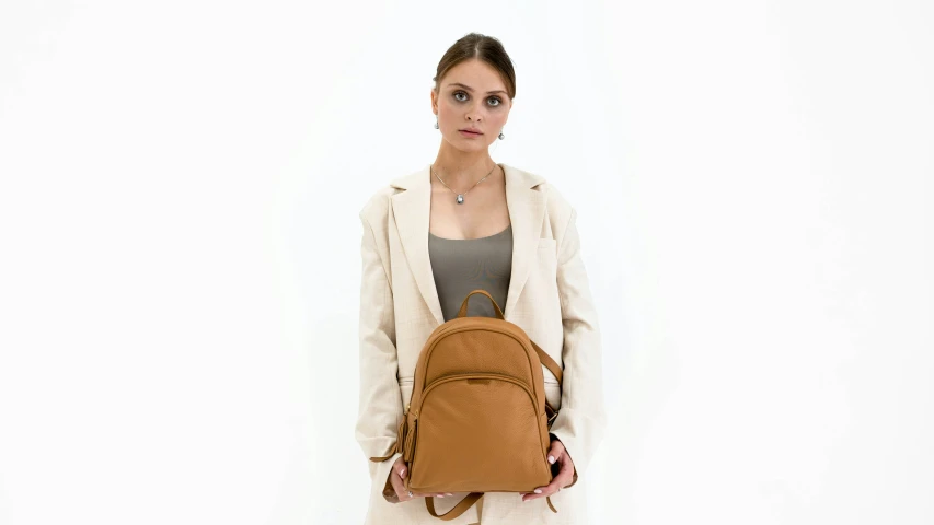 a woman holding a brown backpack, standing