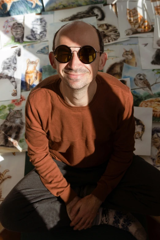 a man wearing sunglasses is sitting in front of a wall with pictures