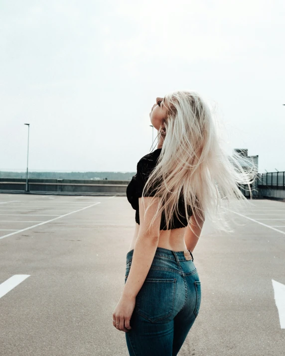 a blonde woman is standing in a parking lot with her head in her hand