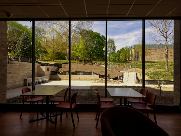 a room with many tables and chairs, outside and a field through the window