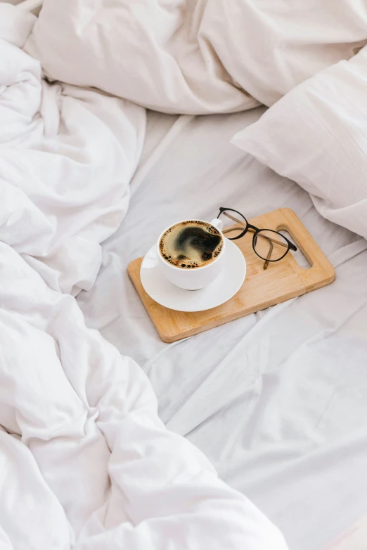 a cup of coffee and glasses on top of a white bed