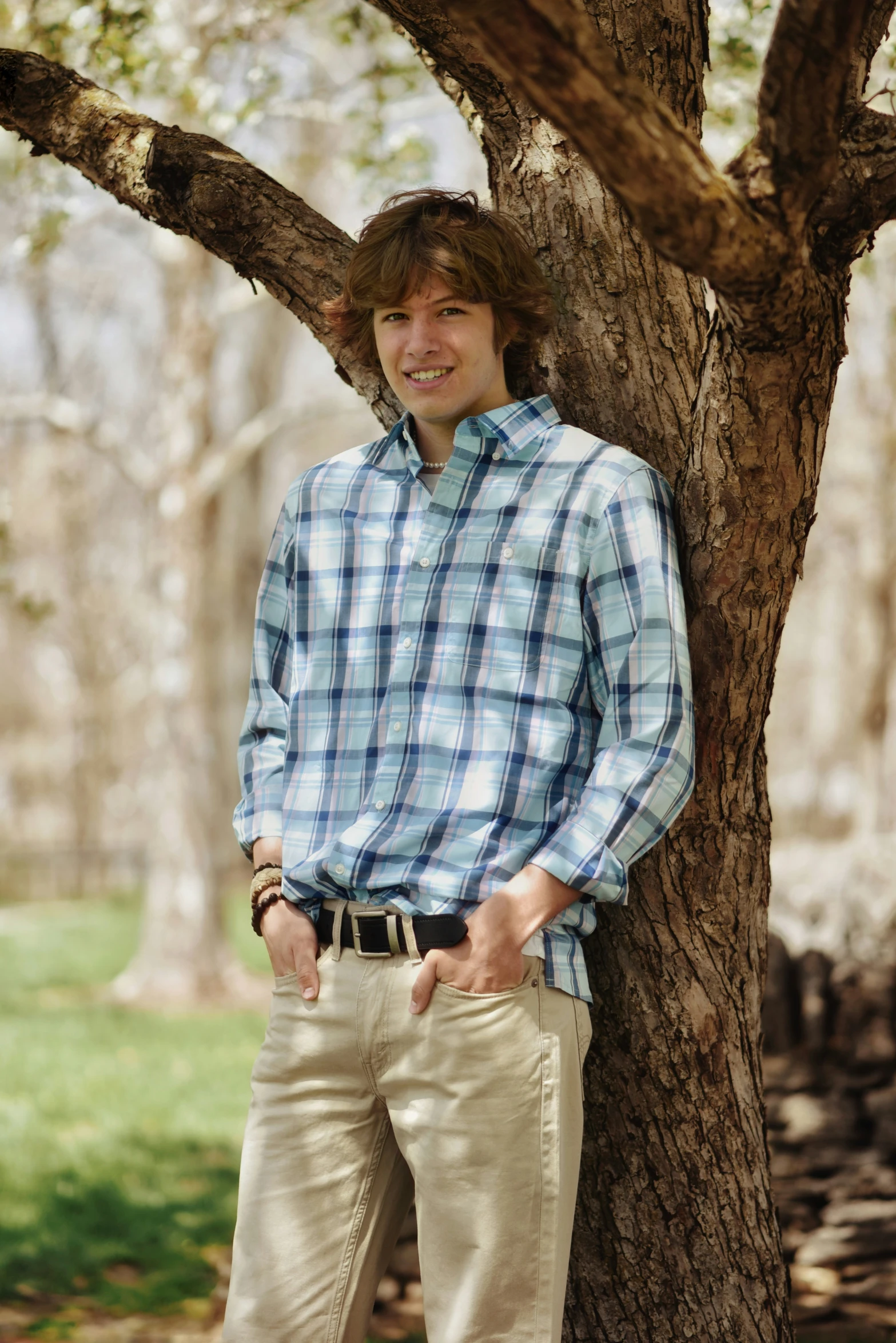 a man standing by a tree looking to his left with both hands in his pockets