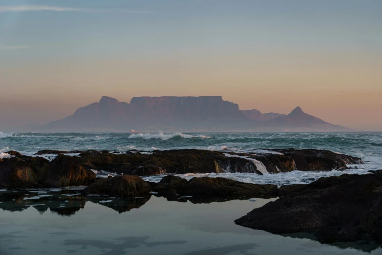 the rocks are in front of the mountain and wave coming from under