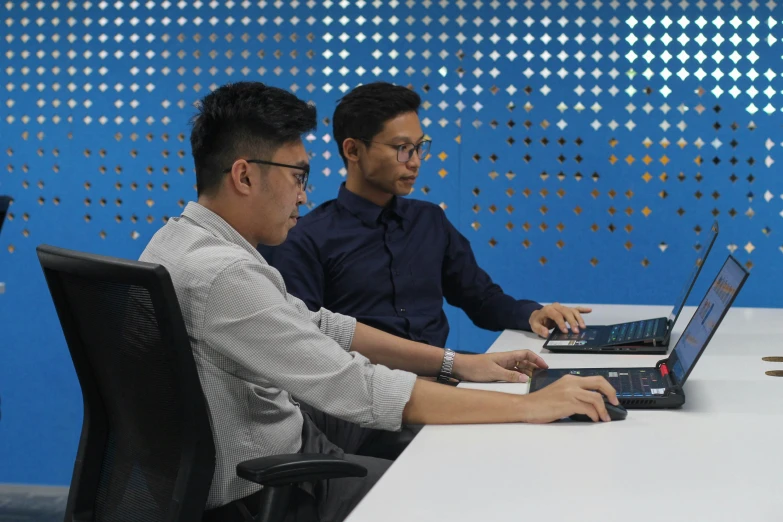 two people sit at tables in front of computers