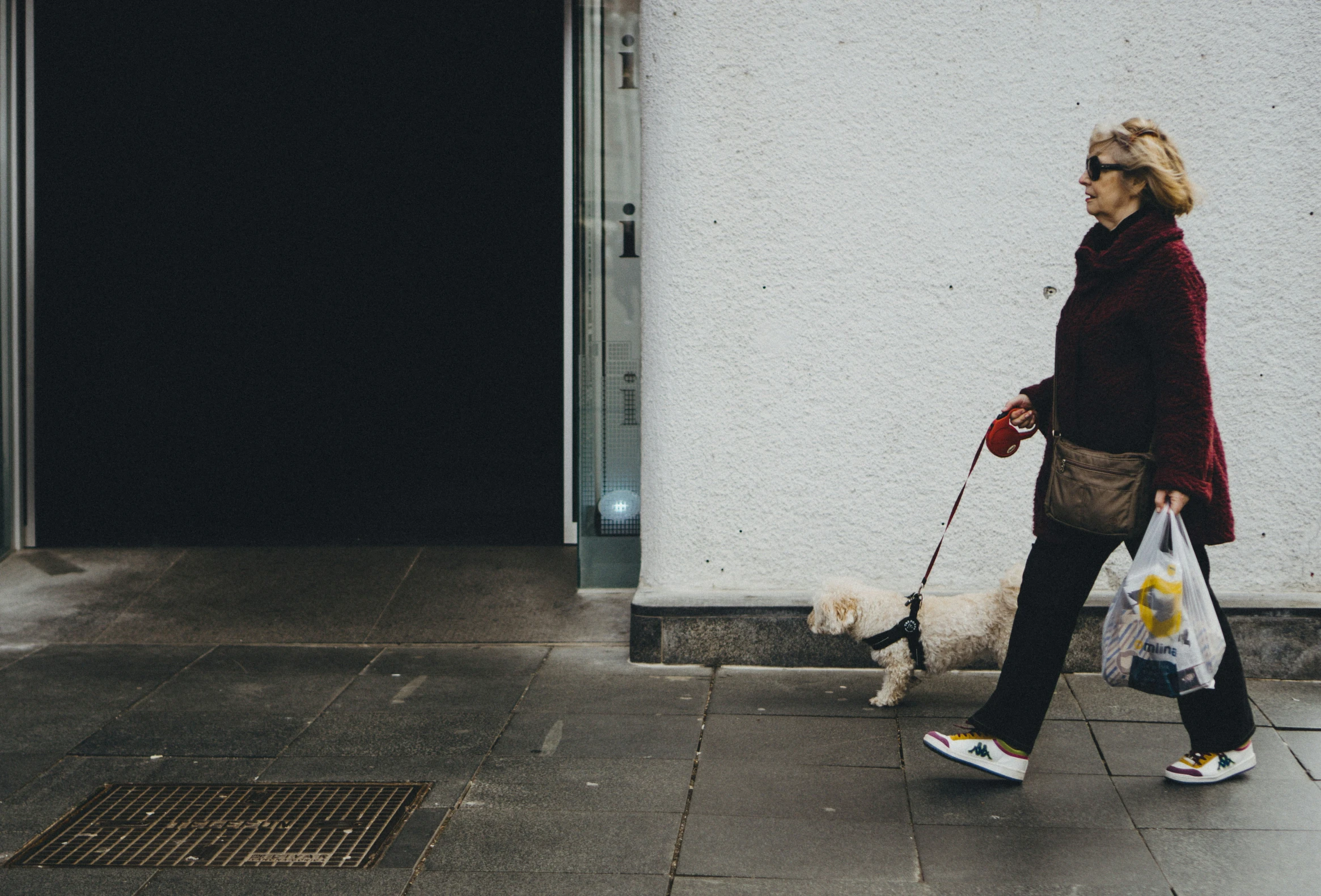 a woman holding two bags walking her dog down the sidewalk