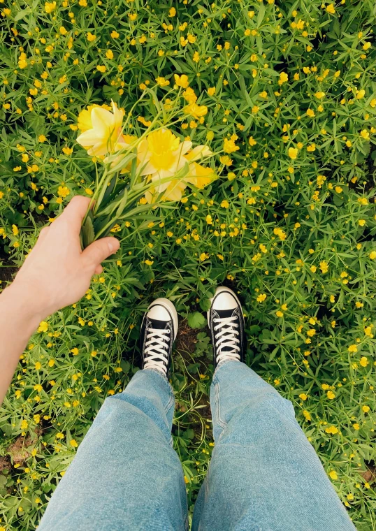 a person in sneakers holding flowers on the grass