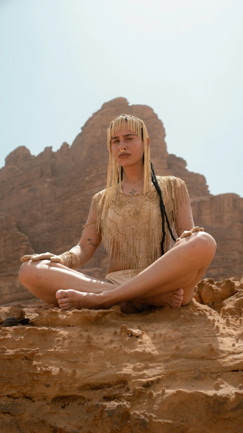 a woman in costume sitting in the desert with her hands on her hip