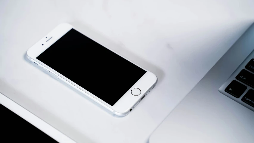 the phone is resting on top of the desk beside the computer