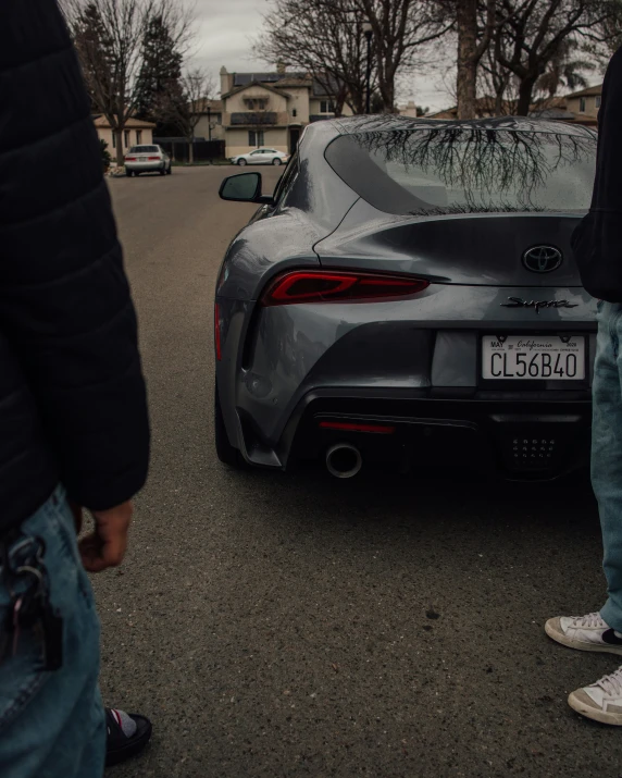 a gray sports car parked in front of a person with jeans on