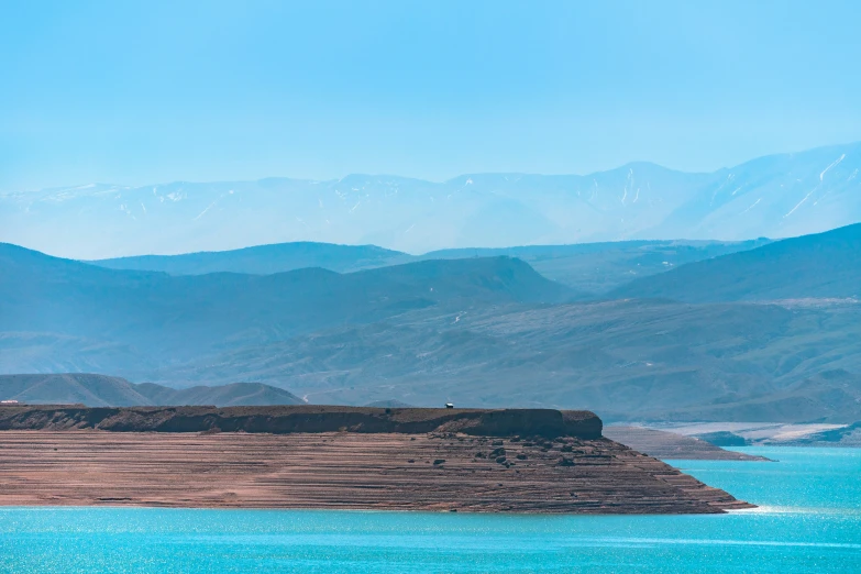 a bird flies across a bright blue water, and mountains in the distance