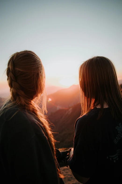 two girls looking at the mountains while standing in the sunset