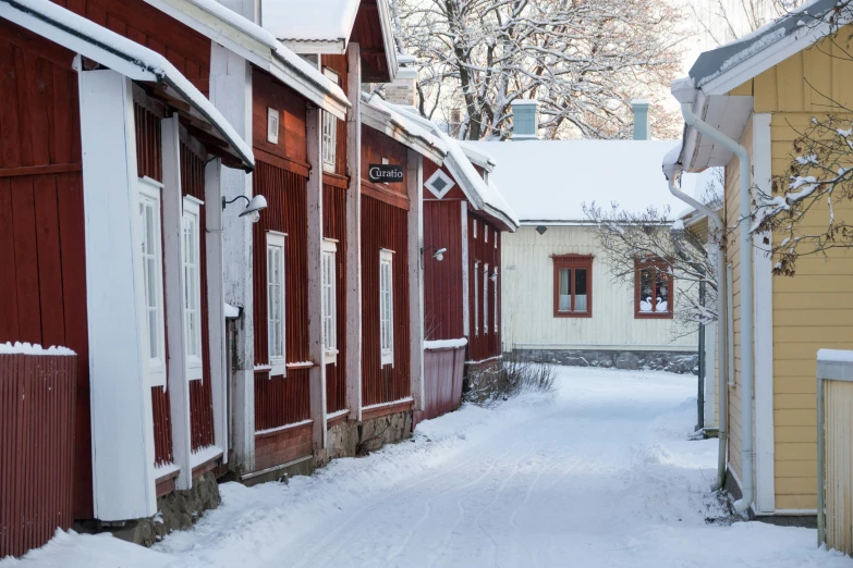 a narrow alley way near red and white wooden houses in the snow